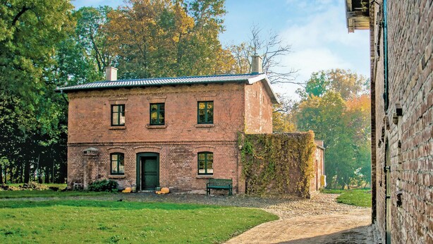 Un edificio de ladrillo con puerta verde, ventanas y un banco al frente.