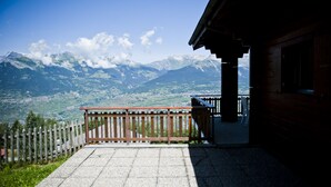 Eine Holzhütte mit einer Steinterrasse mit Blick auf eine gebirgige Landschaft.