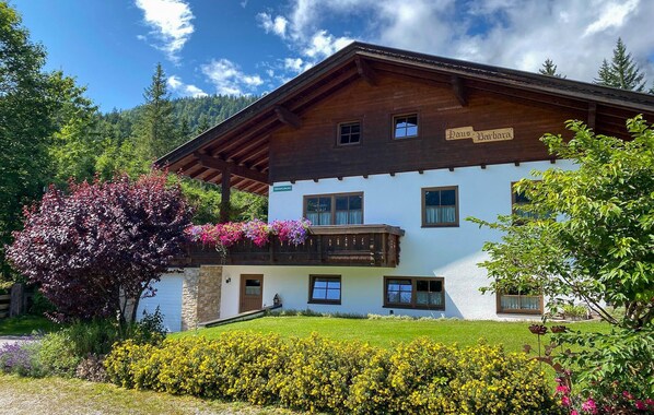 Un chalet traditionnel en bois, doté d’un balcon, d’une enseigne indiquant « Haus Barbara » et d’un jardin bien entretenu.