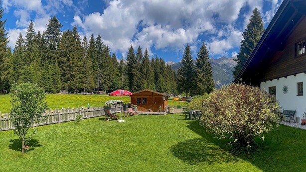 Una cabana de fusta amb un porxo, envoltada per una tanca de fusta, un jardí i un paisatge de muntanya.