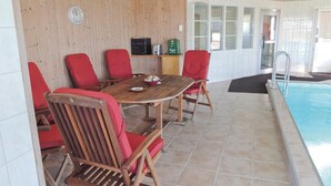 Area piscina con tavolo di legno e sedie rosse, un orologio e una tanica di gas verde su uno scaffale.