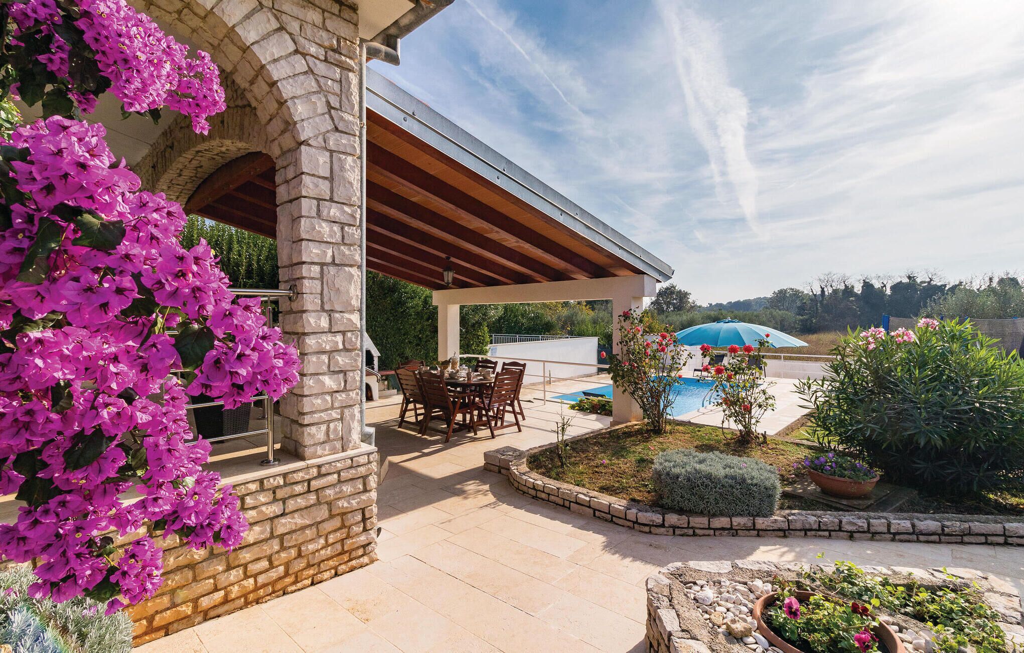 A covered outdoor area with a pool, stone walls, and a patio with chairs and tables.