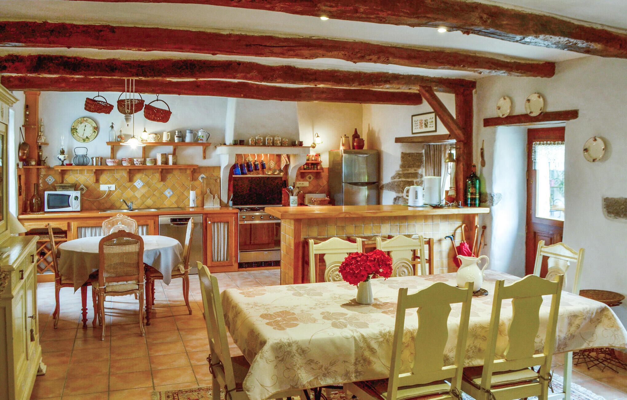 A rustic kitchen with wooden beams, a dining table with chairs, and a refrigerator.