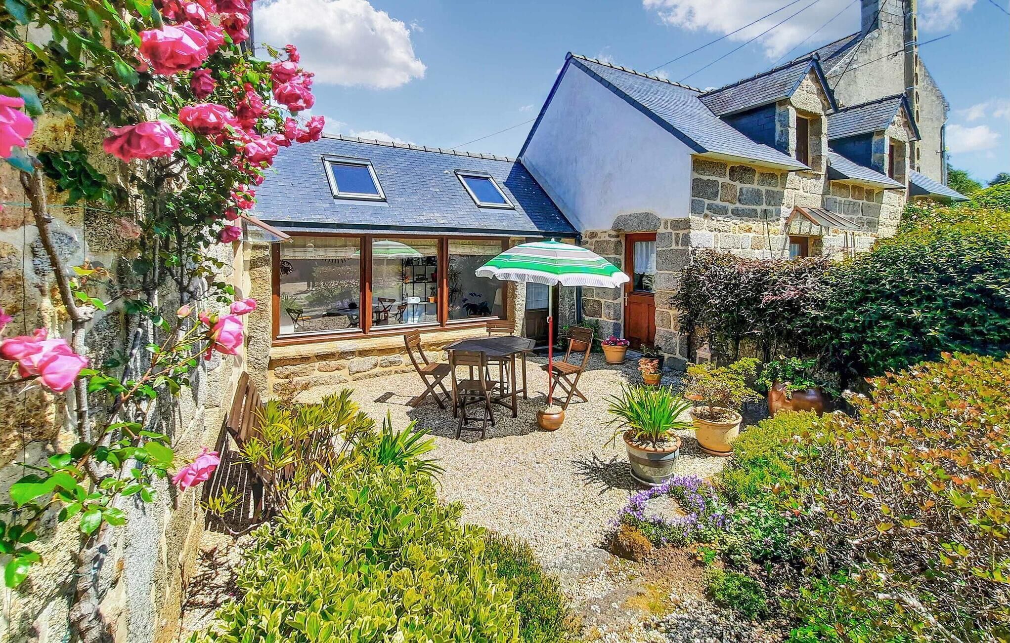 A stone house with a patio, a table, chairs, and a green umbrella.