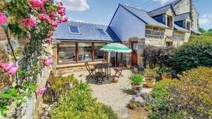 Een stenen huis met een terras, een tafel, stoelen en een groene parasol.
