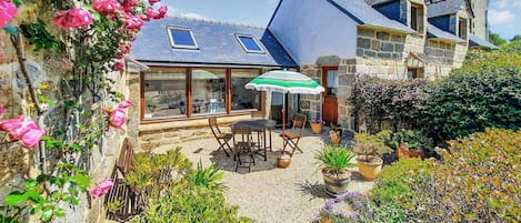 A stone house with a patio, a table, chairs, and a green umbrella.