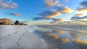 Ein Strand mit blauem Himmel, ruhiger See und Gebäuden im Hintergrund.