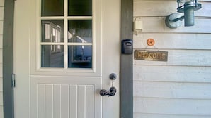 A white door with a window, a doorbell, a wall-mounted light fixture, and a 'Welcome' sign.