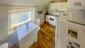 A compact kitchen with white cabinets, a stove, and a refrigerator. There is a window with a view of the outdoors.