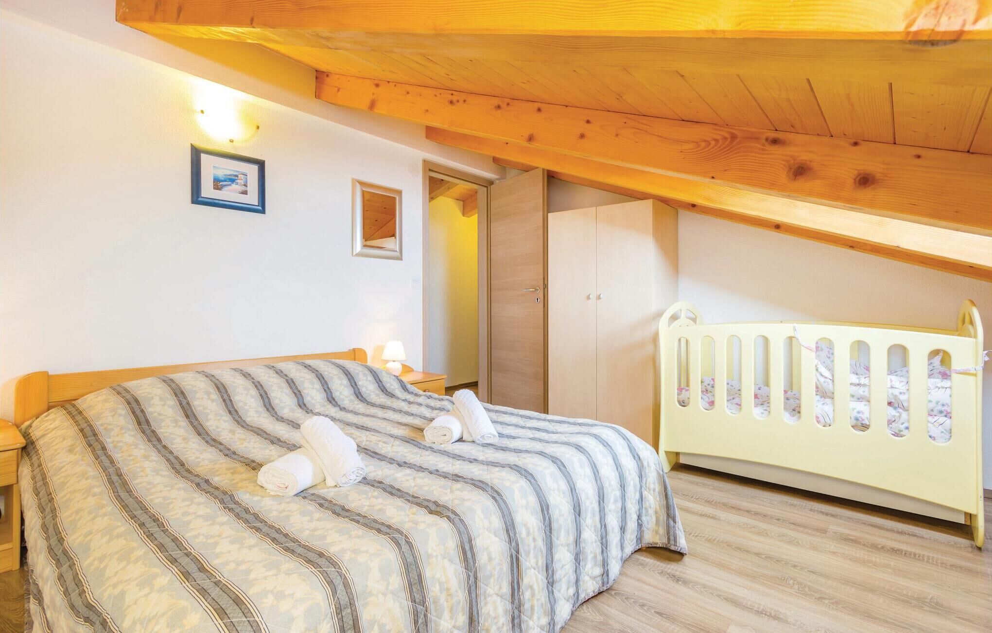 A bedroom with a bed, a crib, wooden beams, a framed picture, and a door.