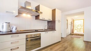 Una cocina moderna con armarios blancos, una campana extractora de acero inoxidable, horno integrado y una cafetera.