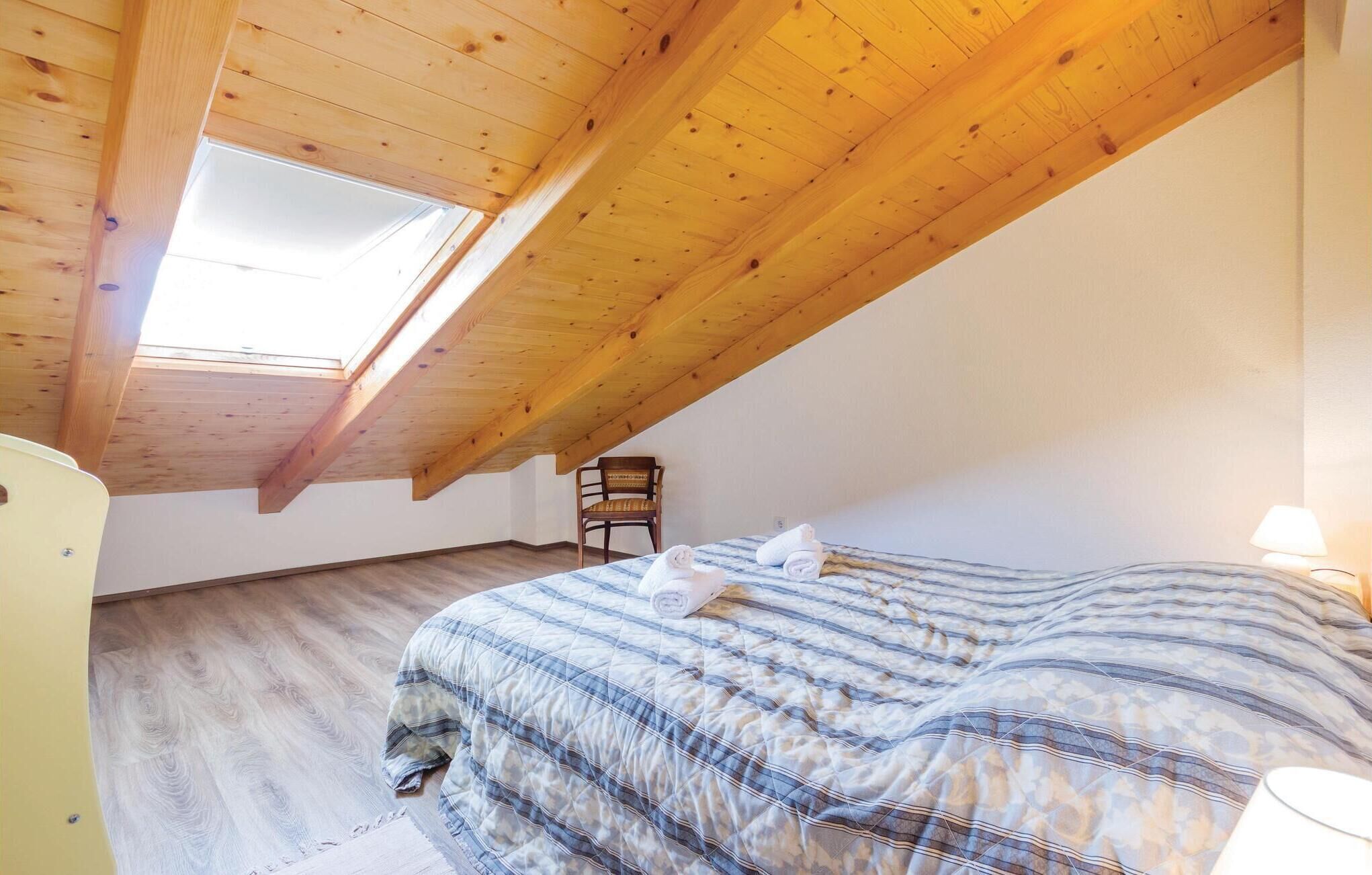 Ein Schlafzimmer mit schrägverdeckter Decke, einem Bett mit gestreifter Bettdecke, einem Stuhl und einer Lampe.