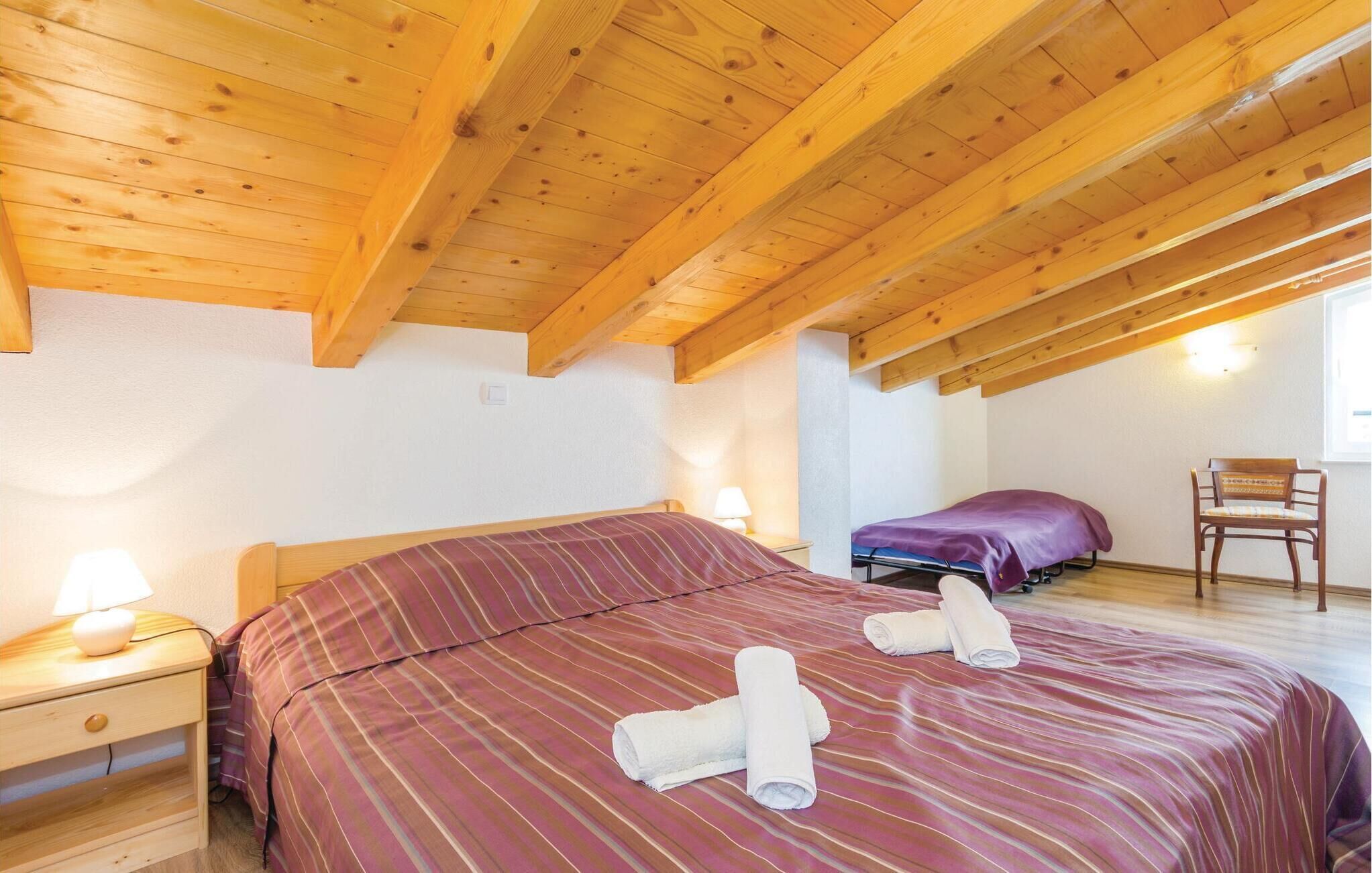 Une chambre avec un plafond en bois, un lit avec une literie à rayures, une chaise et une table de chevet avec une lampe.