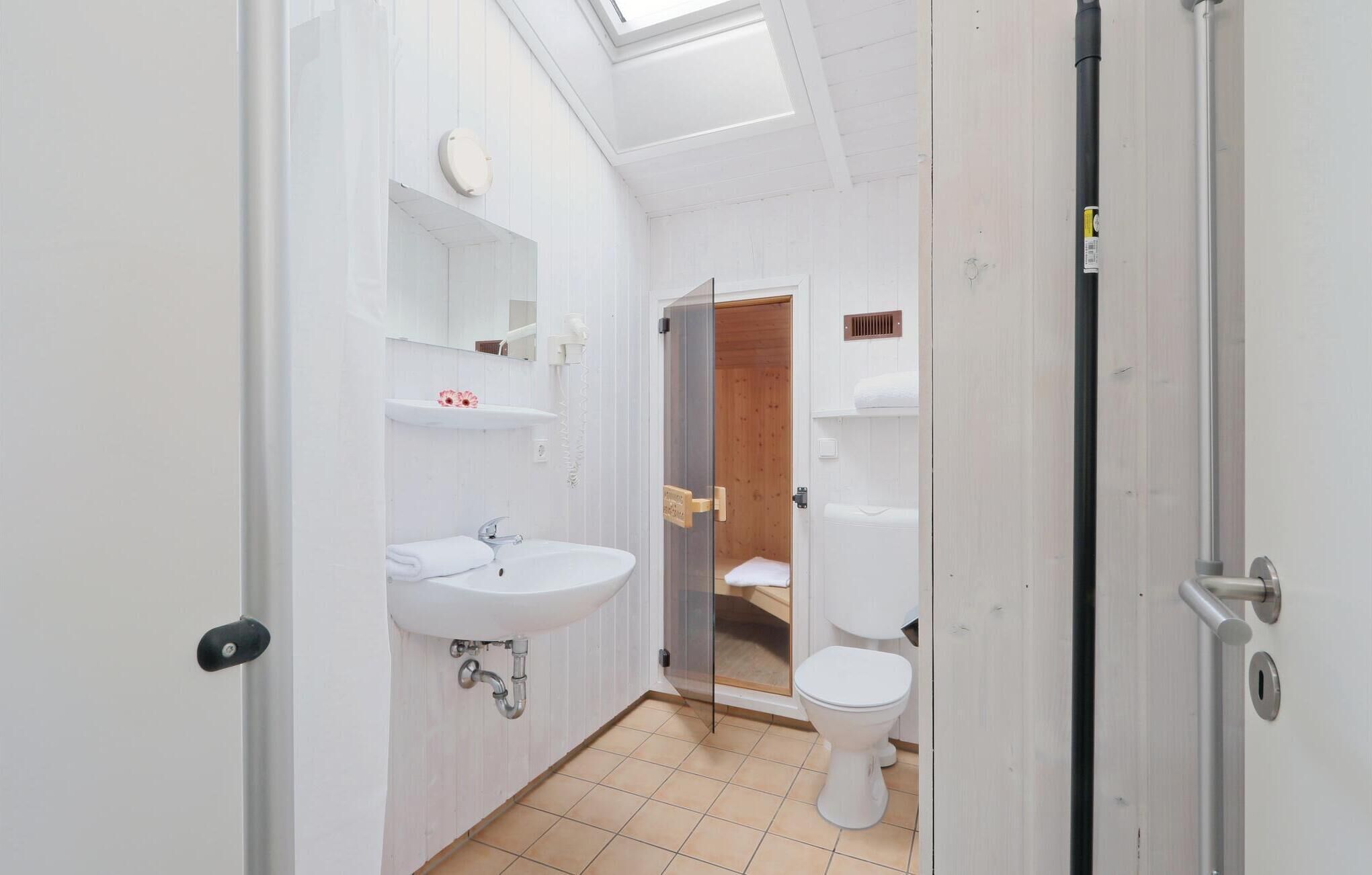 Ein schmales Badezimmer mit einem weißen Waschbecken, einer Toilette und einer Duschkabine.