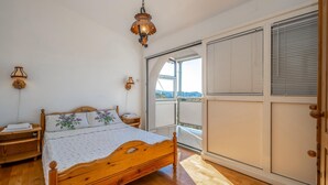 A bedroom with a wooden bed, two wall sconces, a view through a sliding door, and a large window. - Nice home in Klenovica with WiFi (Klenovica)