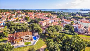 An aerial view of a coastal town with red-roofed buildings, a large body of water, and a prominent villa with a swimming pool. - Amazing home in Medulin (Medulin)