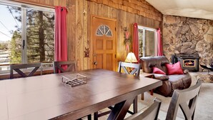 A wooden interior with a dining table, chairs, a fireplace, and a stone wall. - Good Times #1295 (Big Bear City)
