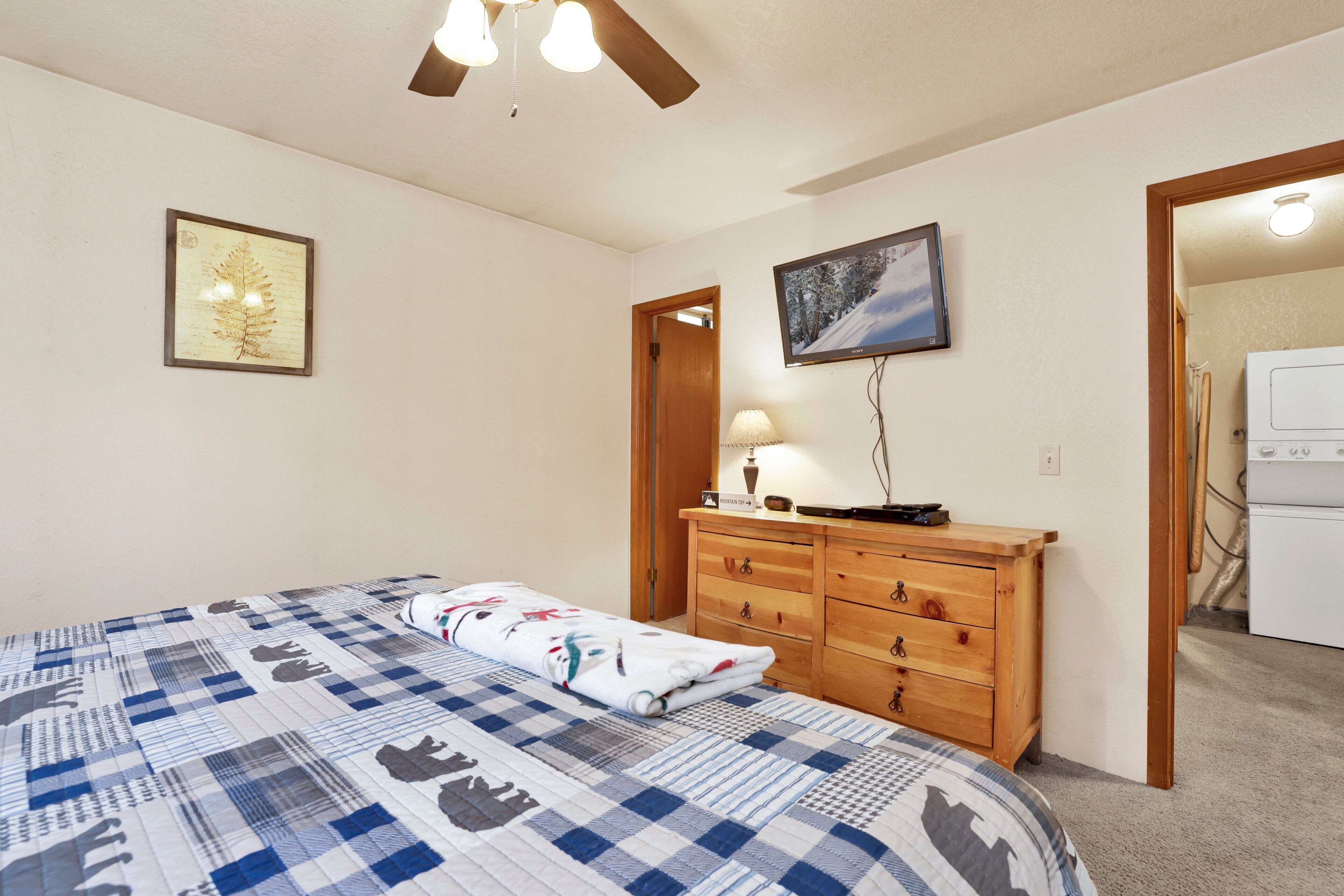 A bedroom with a bed, wooden dresser, and a television on the wall.