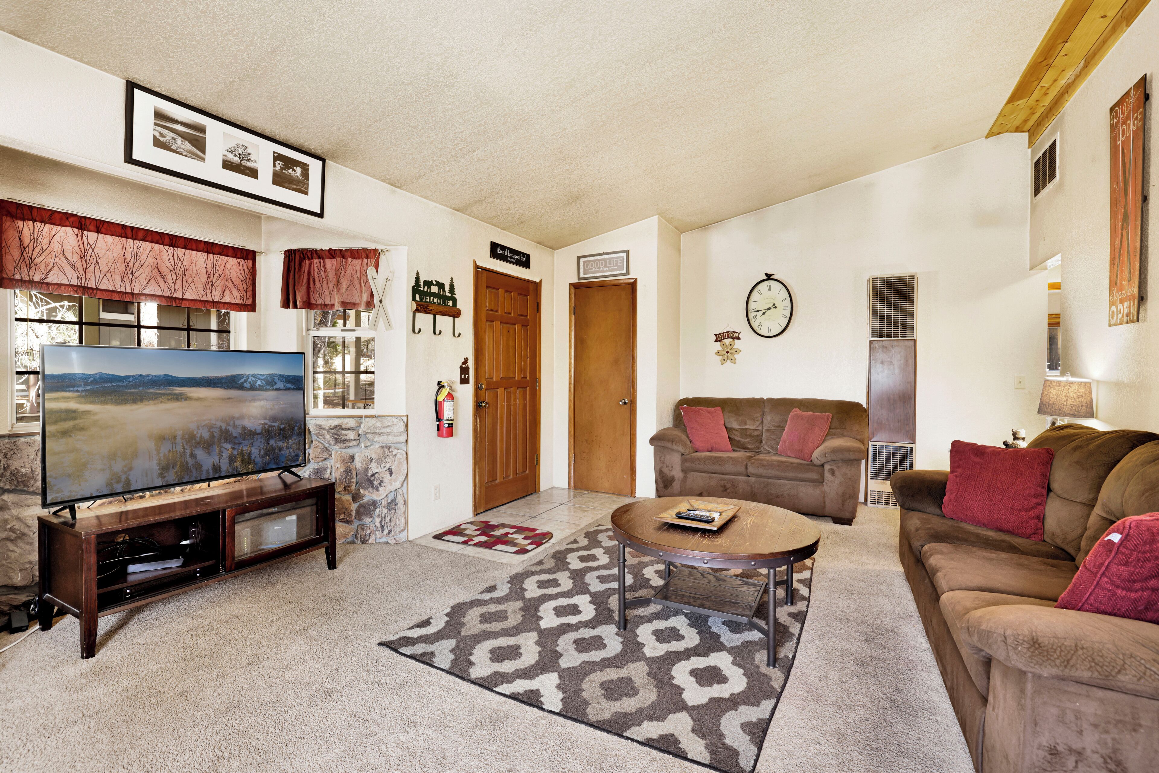 A living room with a flat-screen TV, a wooden entertainment unit, a brown sofa, a round coffee table, and a patterned rug.