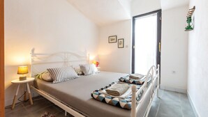 Un dormitorio ordenado con cama, lámparas de noche, una mesita y una puerta que da a otra habitación.