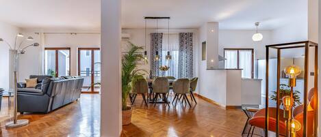 A spacious living area with a wooden floor, a sofa, a dining table with chairs, and a kitchen area with a modern design.