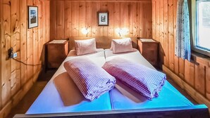 A wooden cabin-style room with a bed, two bedside tables, and two wall-mounted lamps. - Ferienhaus in Maria Luggau (Maria Luggau)