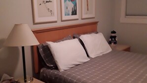 A hotel room with a bed, a nightstand, a lamp, and three framed pictures on the wall. - Fantastic  Spacious Family Condo (Kelowna)