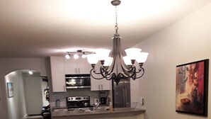 A dining area with a wooden table and chairs, a chandelier, and a kitchen in the background. - Fantastic  Spacious Family Condo (Kelowna)