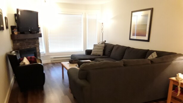 A living room with a dark-colored sofa, a small table, a fireplace, and a framed picture on the wall. - Fantastic  Spacious Family Condo (Kelowna)