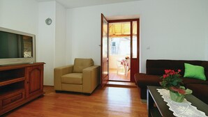 Una sala de estar con un mueble de madera, un sofá beige, un sofá marrón oscuro y un televisor sobre un pedestal de madera.