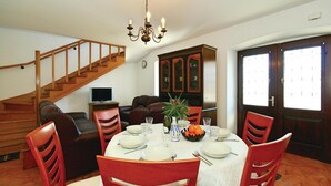 Un comedor con una escalera de madera, una mesa de comedor servida con platos, vasos y un florero con flores.