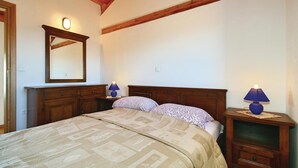 Un dormitorio con una cama grande, cabecera de madera, dos mesitas de noche con lámparas, un espejo y una viga de techo de madera.