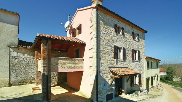 Una casa de piedra de dos pisos con techo de tejas rojas, entrada de ladrillo y una antena parabólica.