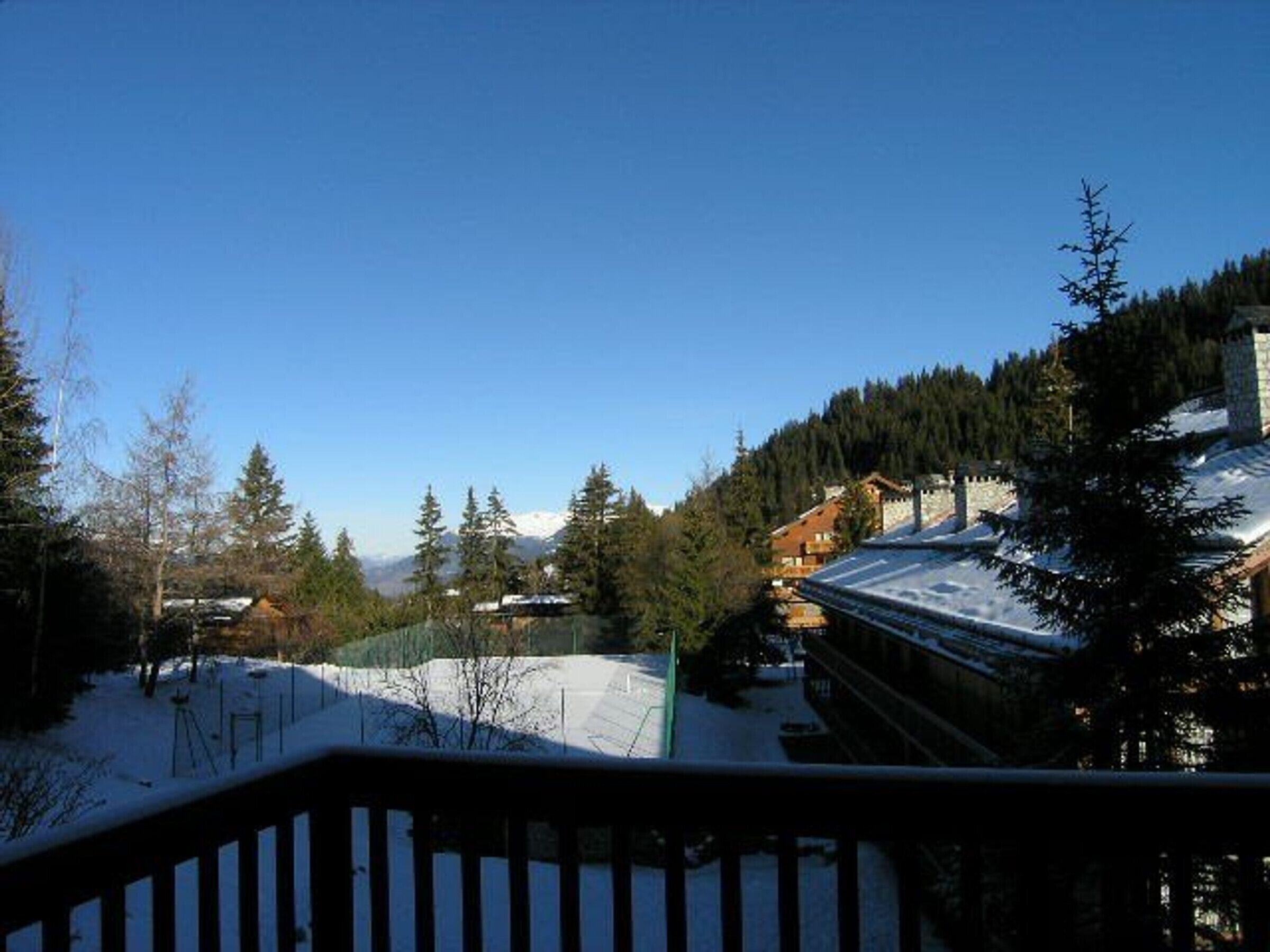 Schneebedeckte Landschaft mit einer Holzterrasse und Blick auf Berg und Wald.
