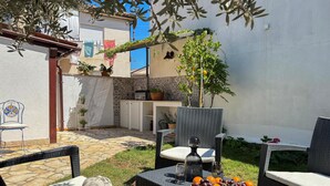 Eine Terrasse mit Korbmöbeln, einem Tisch mit Obst und einer kleinen Küchenzeile.