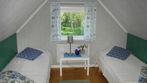 Una habitación pequeña y bien iluminada, con dos camas, una ventana con cortinas, una mesa con lámpara y una planta.