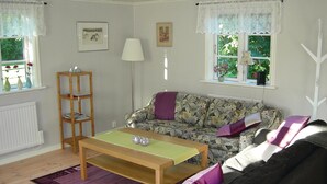 Una sala de estar con un sofá floral, una mesa de centro de madera, una estantería y un radiador.