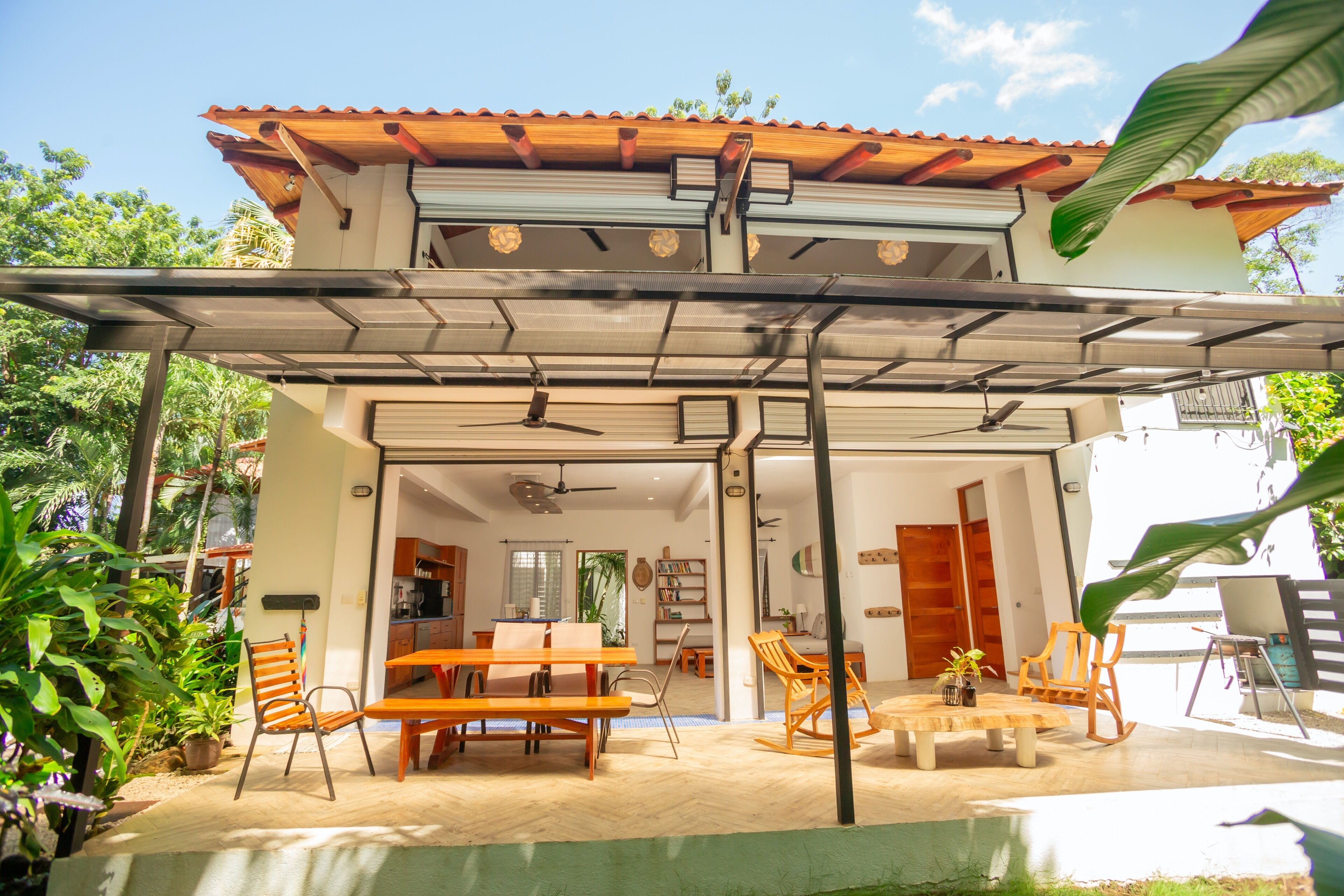 Une maison à deux étages dotée d’un patio couvert, de meubles en bois et offrant une vue sur l’intérieur.