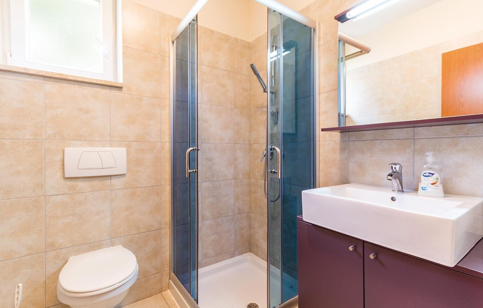 Een moderne badkamer met een douchecabine van glas, een witte wastafel en een toilet.