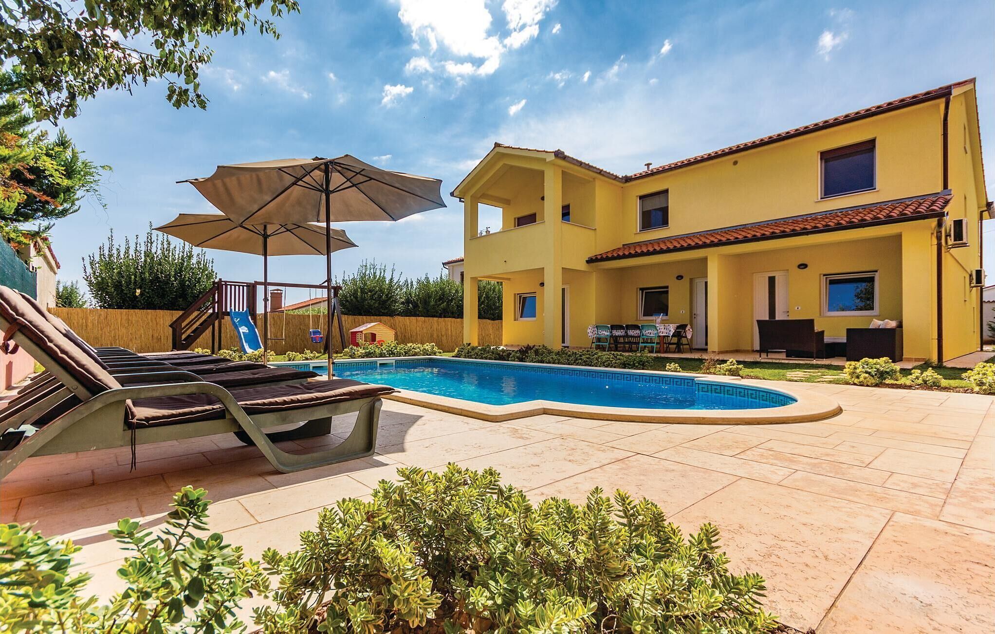A two-story yellow house with a swimming pool, a slide, and outdoor furniture.