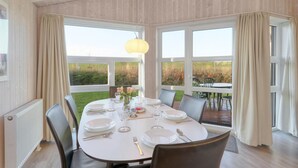 A dining area with a table set for four, large windows, and a view of the outdoors. - Friedrichskoog-Strandpark 9 (Friedrichskoog)