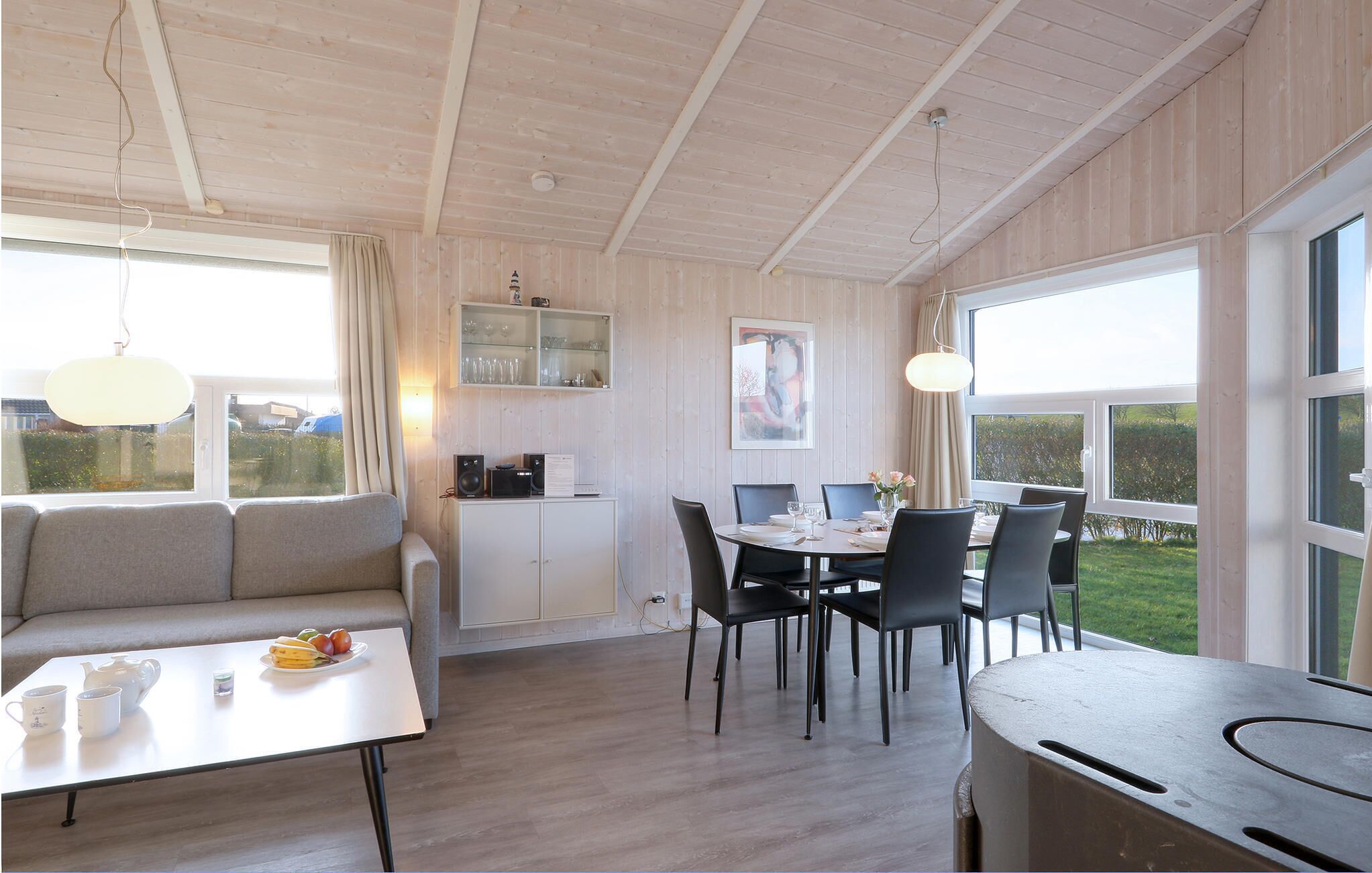 A cozy room with a dining table, chairs, a sofa, and a kitchen area with cabinets and a hanging light fixture.