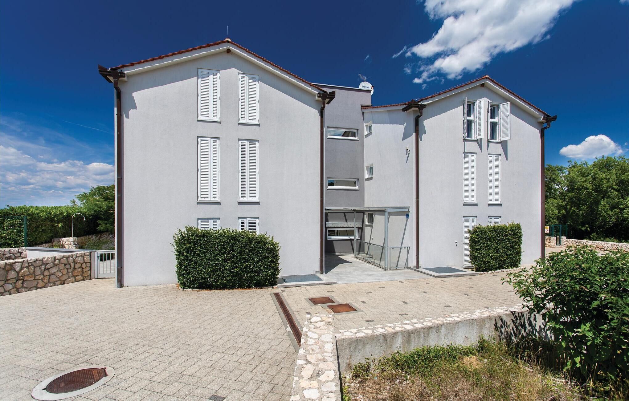 A two-story building with white exterior walls and shutters, a stone foundation, and a paved entrance area with a small garden.
