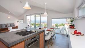 A modern kitchen with a large island, a dining area with white chairs, and a view of the sea.