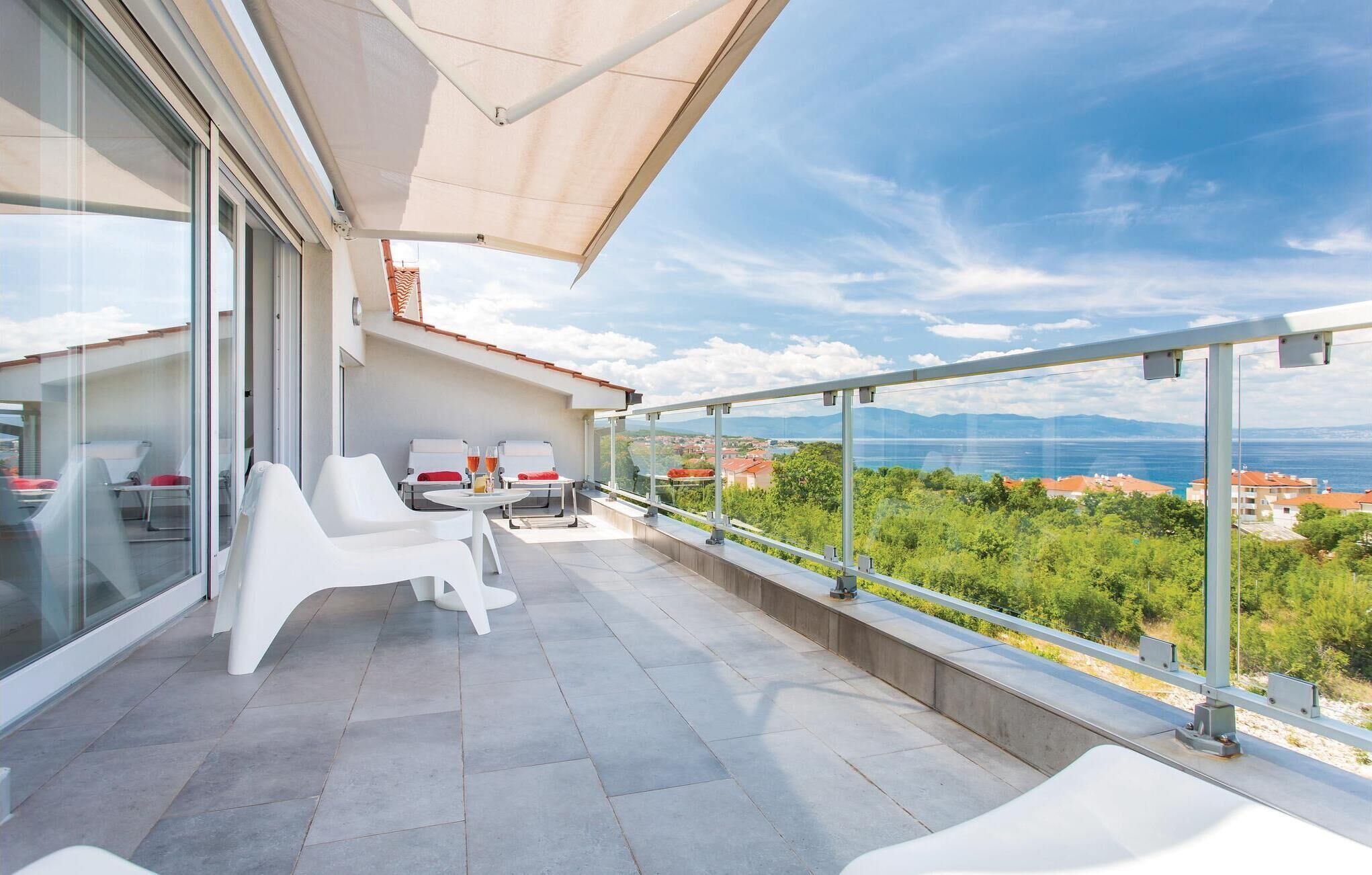 Ein moderner Balkon mit weißer Möbel, einer Glastür und einem herrlichen Blick auf Meer und Berge.