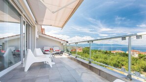 A modern balcony with white furniture, a glass door, and a scenic view of the sea and mountains.