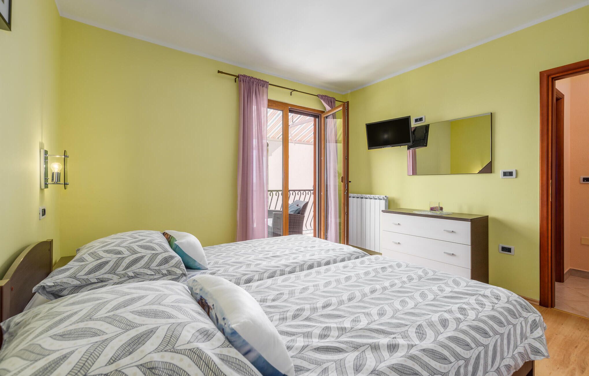 Une chambre avec deux lits, une télévision, une commode et un balcon avec vue.