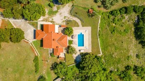 Vue aérienne d’une propriété dotée d’une piscine, d’un bâtiment au toit rouge et d’un espace verdoyant environnant.