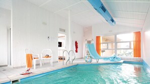 An indoor swimming pool with a blue slide, a diving board, and a poolside chair. - Freibeuterweg 6 - Dorf 6 (Travemünde-Priwall)