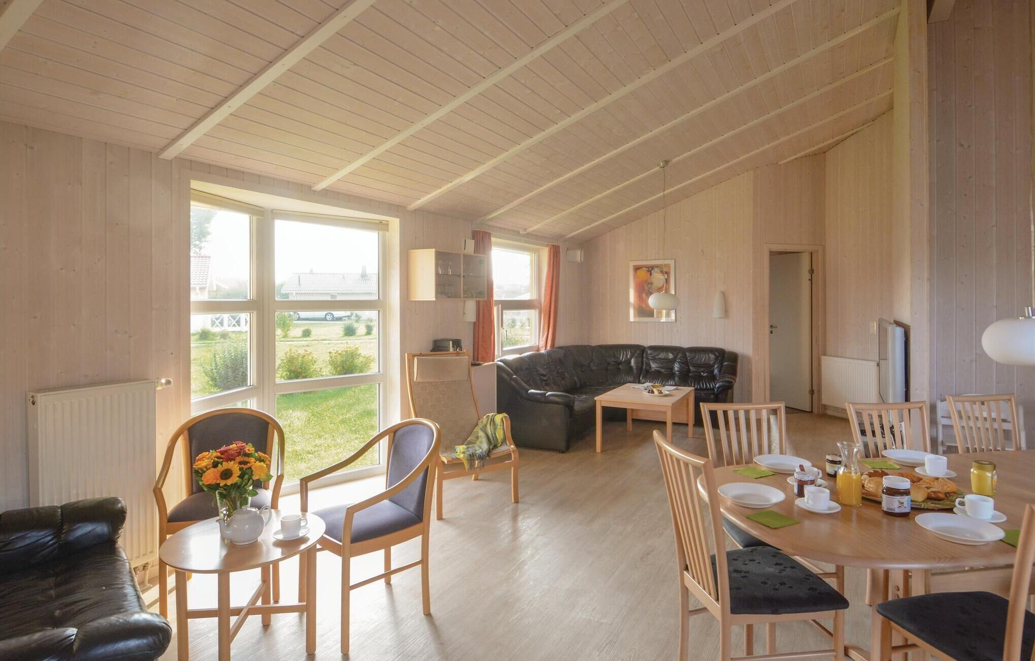 A spacious living room with a black leather sofa, wooden dining table, and chairs. A large window offers a view of the outdoors.